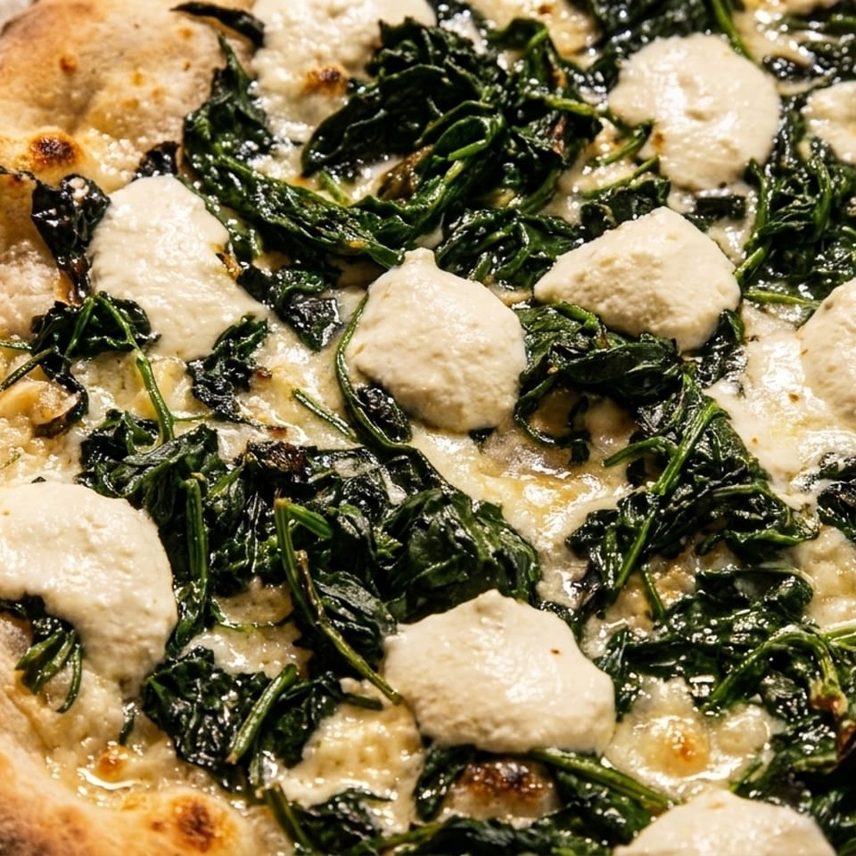 Close-up of a white pizza with spinach and dollops of ricotta cheese on a stone surface.